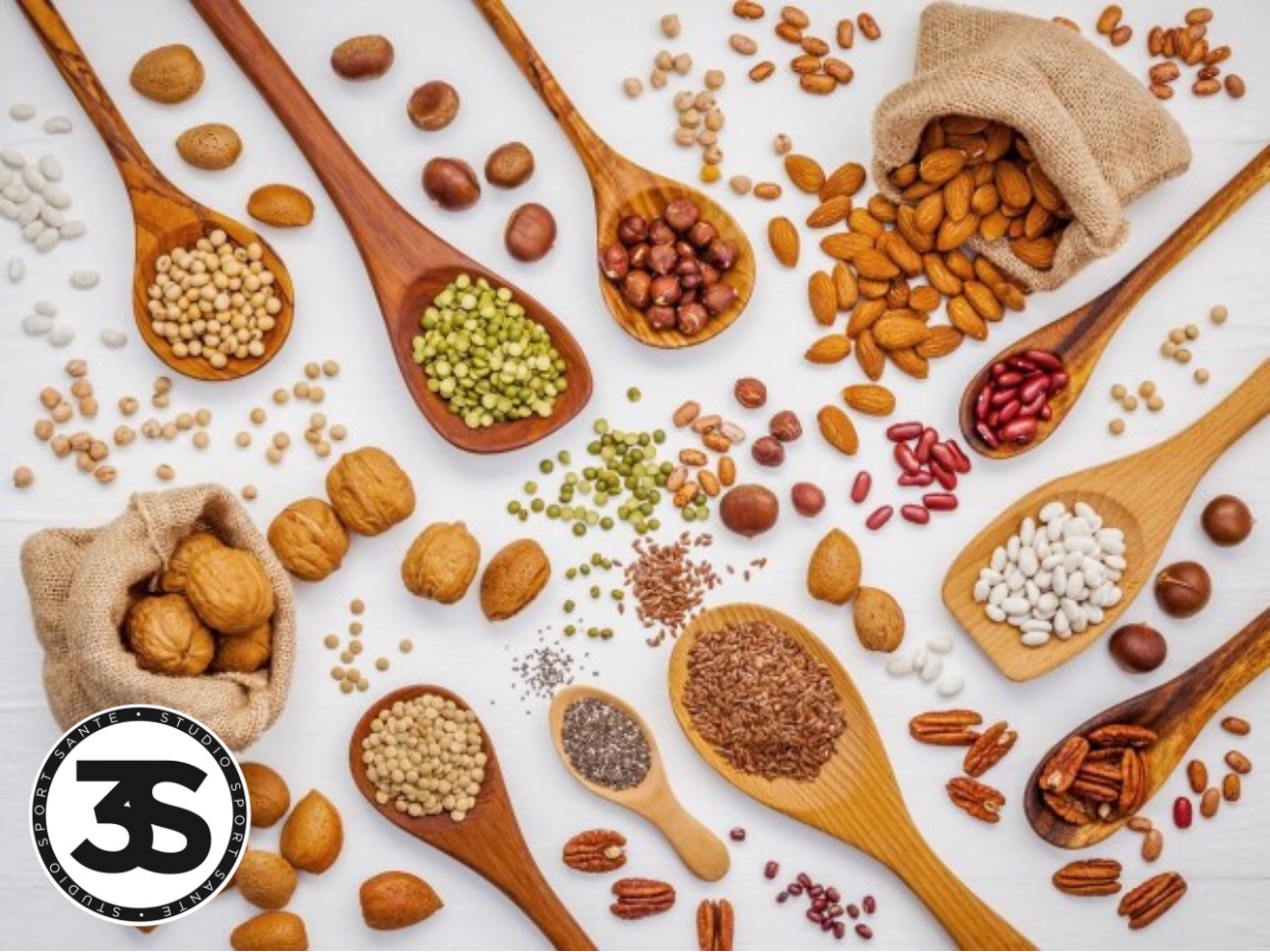 Various legumes and different kinds of nuts in spoons. Walnuts kernels ,hazelnuts, almond ,brown pinto ,soy beans ,flax seeds ,chia ,red kidney beans and pecan set up on white wooden table.